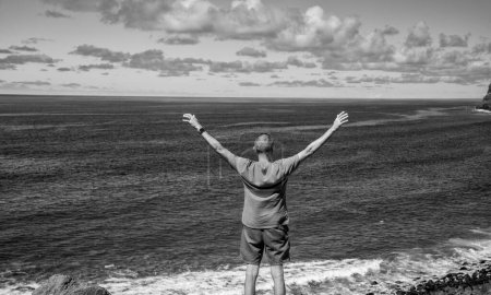 Foto de Hombre con los brazos abiertos abrazando la naturaleza en una hermosa isla, vista trasera. - Imagen libre de derechos
