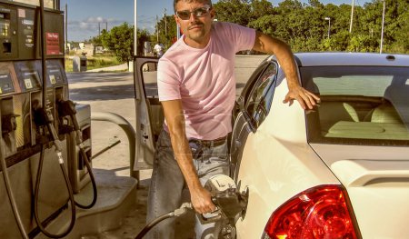 Photo for Happy man holding fuel pump while refueling automobile with benzine at gas station - Royalty Free Image