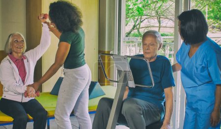 Rehabilitation concept. Elderly retired couple training in a gym supervised by expert african and asian female trainers.