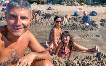 Photo for Happy family of three people building a hot hole in Hot Water Beach, Coromandel, New Zealand. - Royalty Free Image