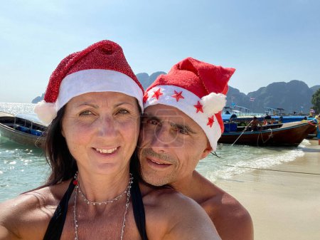 Téléchargez les photos : Noël tropical familial. Couple caucasien portant chapeaux de Noël sur une belle plage. - en image libre de droit