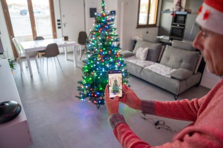 Foto de Hombre que utiliza la aplicación para el hogar inteligente para decorar e iluminar el árbol de Navidad. Vista trasera. - Imagen libre de derechos