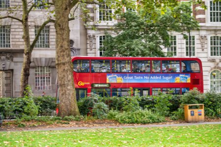 Foto de LONDRES, Reino Unido - JUNIO 2015: Autobús rojo turístico que cruza un parque en Londres. - Imagen libre de derechos
