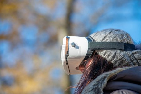 Téléchargez les photos : Femme heureuse portant une visière de réalité virtuelle explorant le parc de la ville. - en image libre de droit