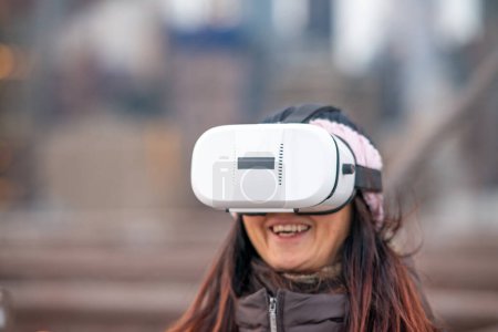 Foto de Mujer feliz vistiendo un visor de realidad virtual explorando la ciudad. - Imagen libre de derechos