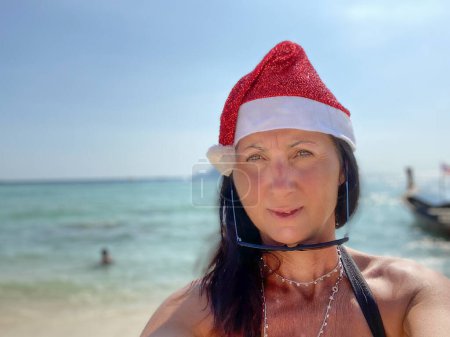 Téléchargez les photos : Noël tropical familial. Heureuse femme caucasienne portant chapeau de Noël sur une belle plage. - en image libre de droit