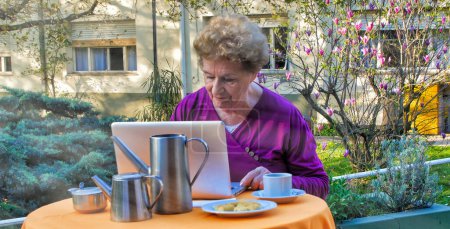 Téléchargez les photos : Les personnes âgées ritered femme heureuse parlant sur un vidéocall en face d'un ordinateur portable dans le jardin. Concept de retraite. - en image libre de droit