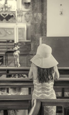 Photo for Woman wearing straw hat praying inside a church, back view. Religion and Christian concept. - Royalty Free Image