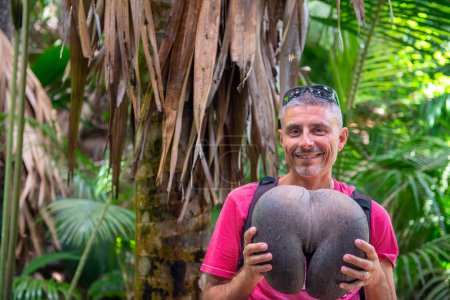 Man embracing Coco De Mer along a beautiful tropical trail, Vallee de Mai.
