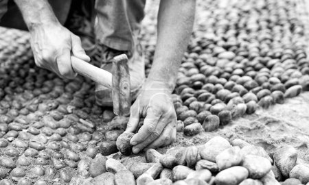 Photo for Road works. Man puts pebbles on the old road with the hammer. - Royalty Free Image