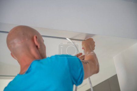Photo for Worker installs a new led strip into a drywall ceiling. New house illumination system. - Royalty Free Image