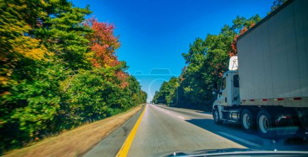 American style truck on freeway pulling load. Transportation theme. Giant truck along New England in autumn.