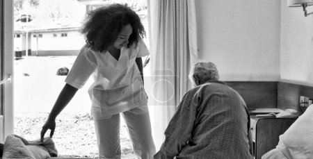Photo for Young african female doctor helping elderly retired man in the hospital bed. - Royalty Free Image
