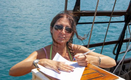 Téléchargez les photos : Portrait d'une femme caucasienne d'affaires heureuse en maillot de bain signant des documents sur le bateau. - en image libre de droit