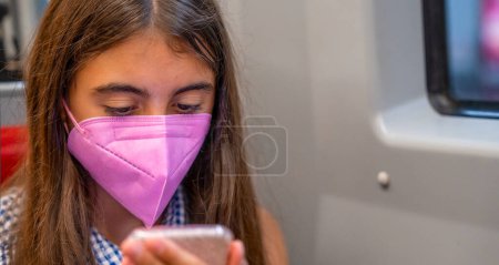 Foto de Chica joven en el tren del metro con máscara rosa y el uso de teléfono inteligente. - Imagen libre de derechos