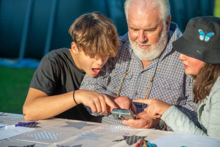 Photo for Grandfather reviewing images from a compact camera outdoor with his grandchildren - Royalty Free Image