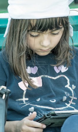 Téléchargez les photos : Jeune fille relaxante avec tablette assise sur un banc de parc de la ville. - en image libre de droit