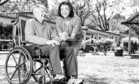 Foto de Asiática enfermera feliz con caucásico anciano paciente en silla de ruedas, vista al aire libre. - Imagen libre de derechos