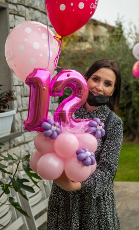 Téléchargez les photos : Fille caucasienne tenant anniversaire ballons d'hélium pour sa fille fête. - en image libre de droit