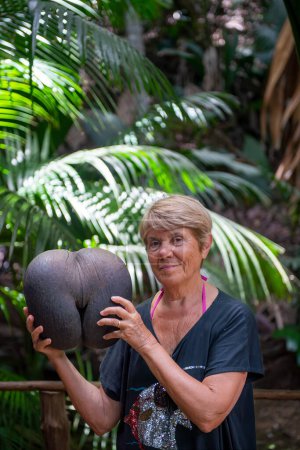 Téléchargez les photos : Elderly woman embracing Coco De Mer along a beautiful tropical trail, Vallee de Mai. - en image libre de droit