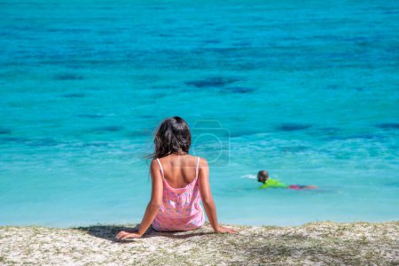 Téléchargez les photos : Jeune fille regardant vers la mer avec l'homme nageant en arrière-plan. - en image libre de droit