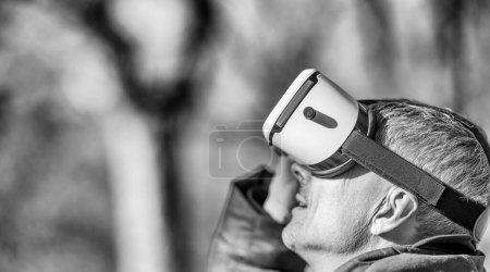 Téléchargez les photos : Homme heureux portant une visière de réalité virtuelle explorant le parc de la ville. - en image libre de droit