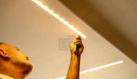 Téléchargez les photos : Led strip with yellow warm light, light installation. Male installer. - en image libre de droit