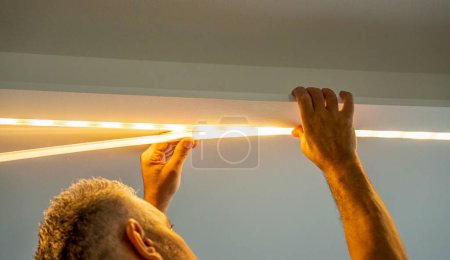 Téléchargez les photos : Installation de la bande LED pour l'éclairage correctement sur la surface de l'armoire sur l'ensemble de cuisine. - en image libre de droit