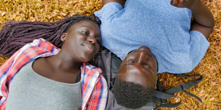 Téléchargez les photos : Couple adolescent africain couché sur l'herbe en utilisant une tablette et relaxant. Concept de bonheur et de légèreté. - en image libre de droit