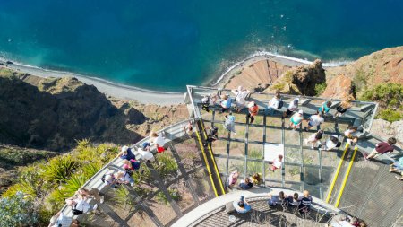 Foto de Tourists enjoy the viewpoint at Cabo Girao, along the Madeira coastline, Portugal. Aerial view from drone. - Imagen libre de derechos