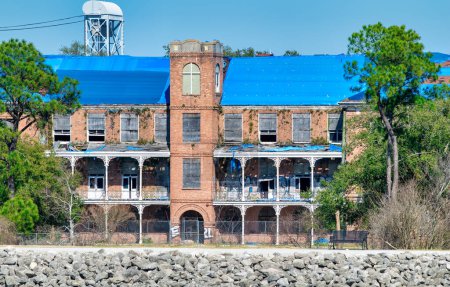 Photo for New Orleans, LA - February 11, 2016: A rustic abandoned warehouse on the shoreline as viewed on a boat while traveling along the Mississippi River. - Royalty Free Image