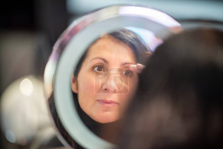 Téléchargez les photos : Attrayant femme faisant maquillage quotidien tout en se tenant près du miroir. - en image libre de droit