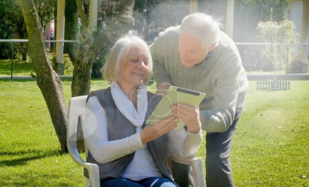 Téléchargez les photos : Heureux couple retraité utilisant gadgets tech en plein air sur une journée ensoleillée. - en image libre de droit