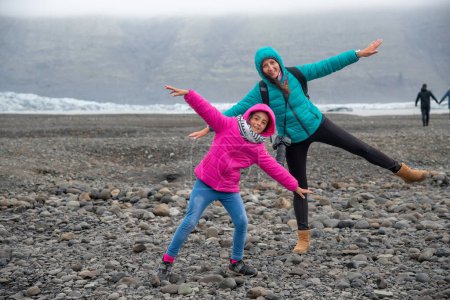 Foto de Madre e hija imitando volar en la playa de Jokulsarlon, Islandia. - Imagen libre de derechos