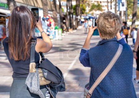 Photo for Two women of different ages together photographing city street life on a sunny day. - Royalty Free Image