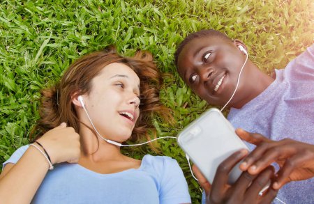 Foto de Pareja multiétnica de adolescentes acostados en el césped escuchando música. Concepto de felicidad y ligereza. - Imagen libre de derechos