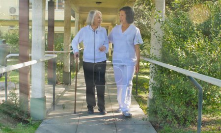 Foto de Médico asiático que ayuda a las mujeres mayores jubiladas con bastón de paseante en el patio del hospital. Concepto de rehabilitación. - Imagen libre de derechos