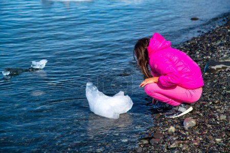 Téléchargez les photos : Jeune fille touchant un petit morceau de glace dans la lagune de Jokulsarlon. - en image libre de droit