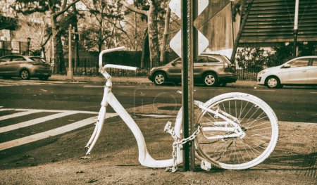 Téléchargez les photos : Vélo blanc abandonné avec une roue enchaînée à un poteau le long d'une rue de la ville - en image libre de droit