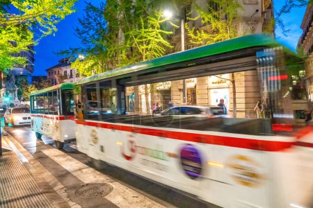 Foto de Granada, España - 13 de abril de 2023: El tranvía urbano se acelera por las calles de la ciudad por la noche. - Imagen libre de derechos