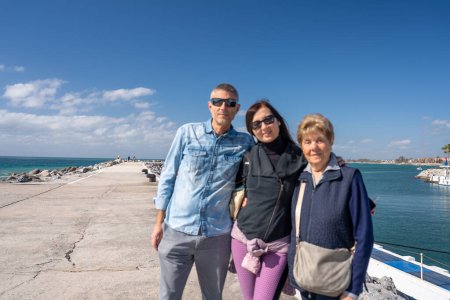 Téléchargez les photos : Une retraitée âgée en vacances avec sa fille et son fils, un port de la ville en arrière-plan. - en image libre de droit