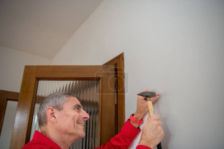 Photo for A man puts a nail in the wall to hang a picture. - Royalty Free Image