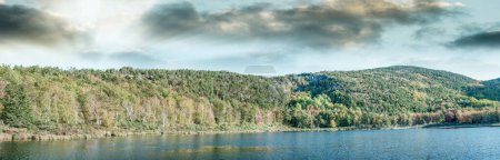 Photo for Panoramic aerial view of lake and trees in autumn foliage seaon against blue sky. - Royalty Free Image