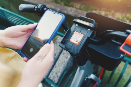 Téléchargez les photos : Fille prend un vélo loué dans un parking à vélos avec smartphone - en image libre de droit