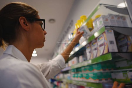 Téléchargez les photos : Pharmacist arranges medicine on the shelve in the pharmacy - en image libre de droit
