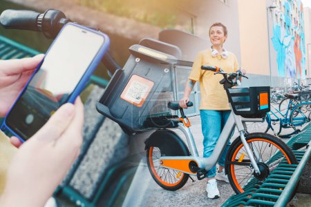 Foto de Chica toma una bicicleta alquilada en un aparcamiento de bicicletas con teléfono inteligente - Imagen libre de derechos
