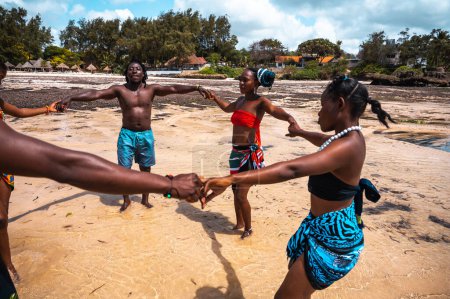 Foto de Amigos kenianos bailan en la playa con ropa típica local - Imagen libre de derechos