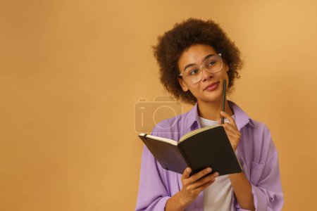 Téléchargez les photos : Afro femme pense quelque chose avec livre à la main - en image libre de droit