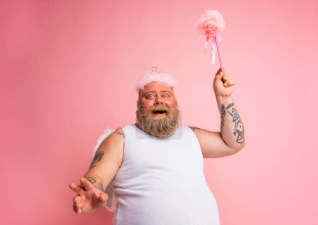Téléchargez les photos : Gros homme avec des tatouages et de la barbe agit comme une fée magique fan - en image libre de droit
