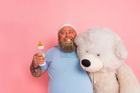 Photo for Man acts like a child with pacifier, baby bottle and a big teddybear - Royalty Free Image
